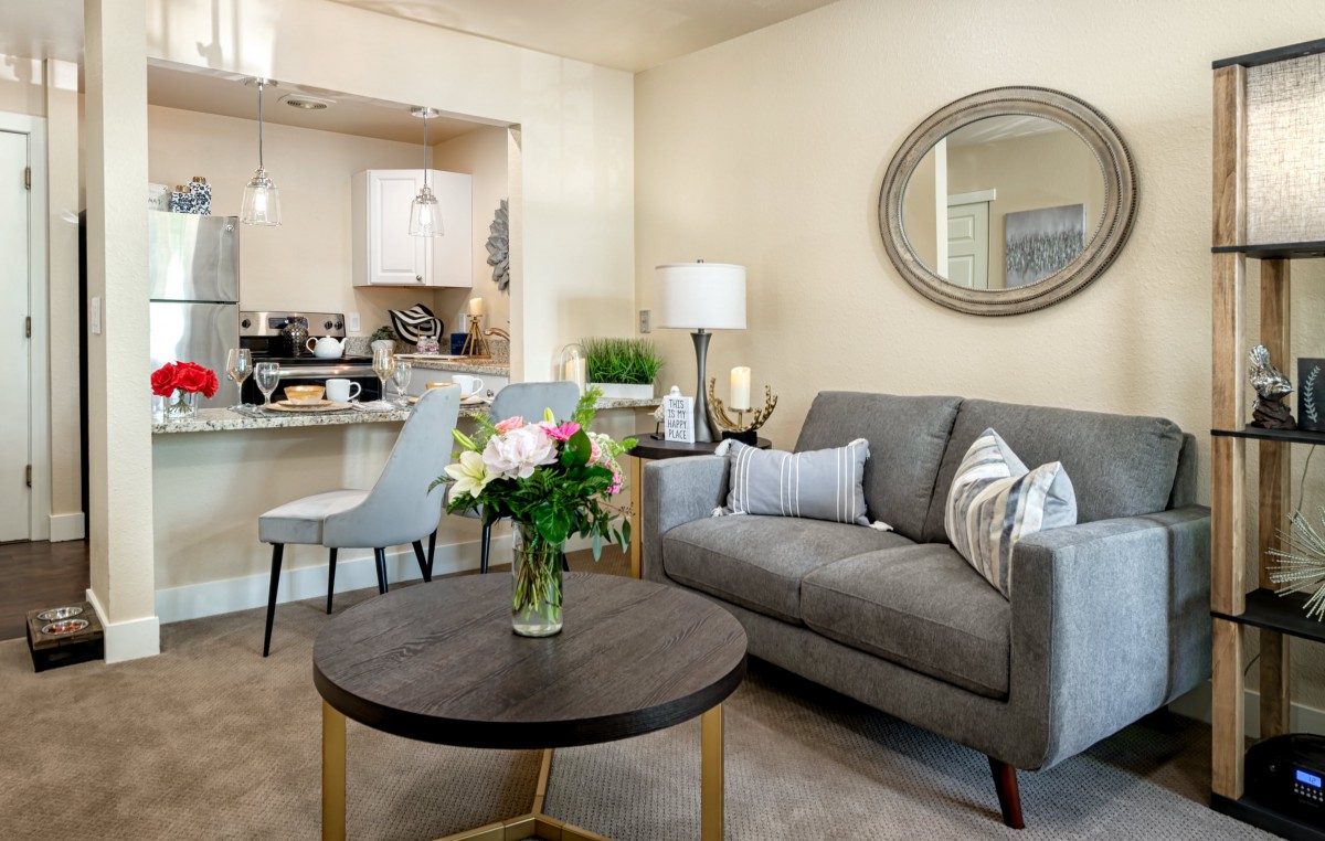 A modern living room with a cozy sofa, round coffee table, and decorative elements including flowers and a mirror.