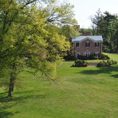 A brick house surrounded by a large, green lawn and trees in a peaceful setting.