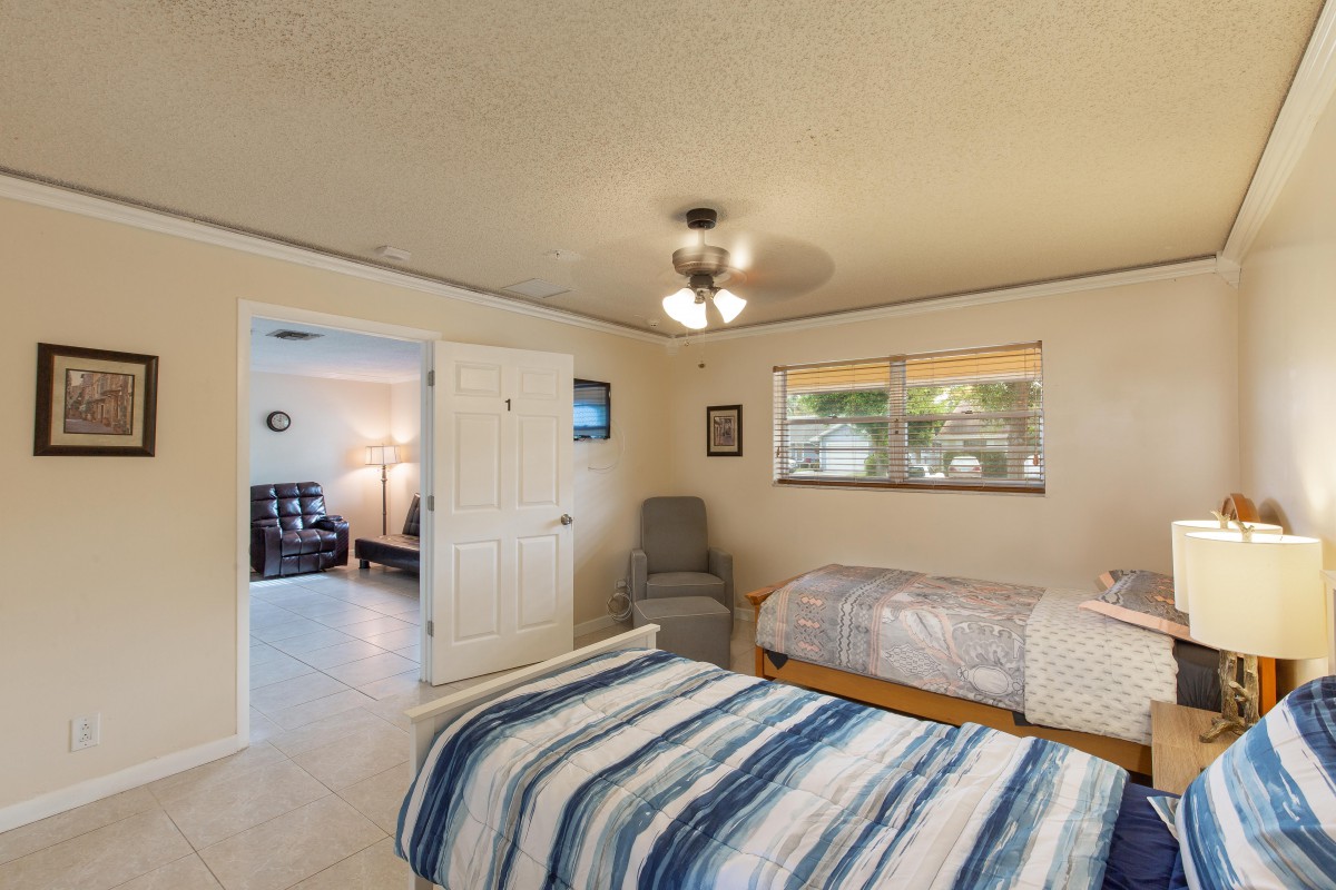 A cozy bedroom with two beds, a chair, and a ceiling fan.