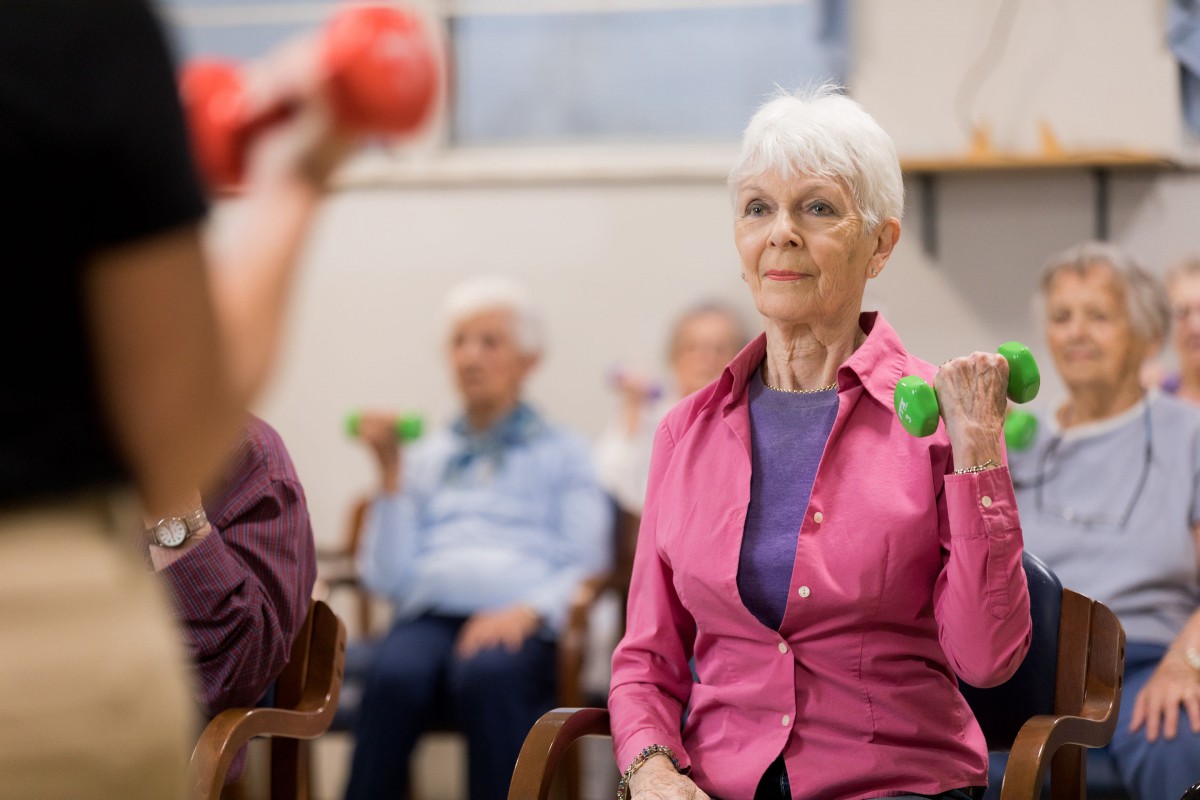 A group of seniors participating in a fitness class, lifting small weights.