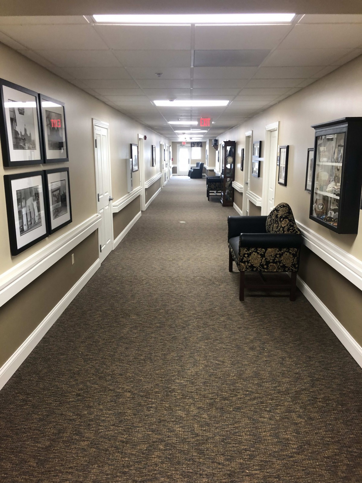 A long, carpeted hallway with seating areas and framed pictures on the walls.