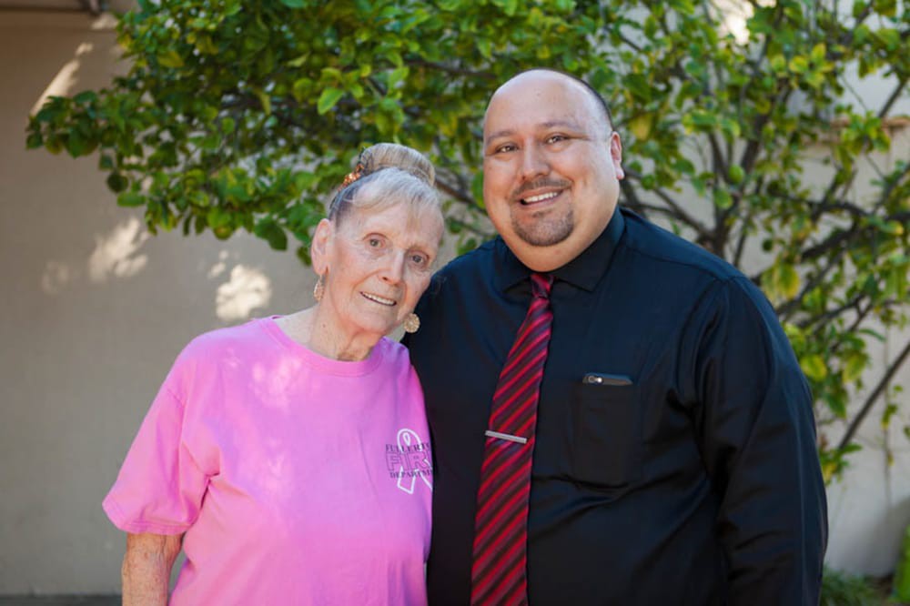 A smiling elderly woman and man standing together outdoors.