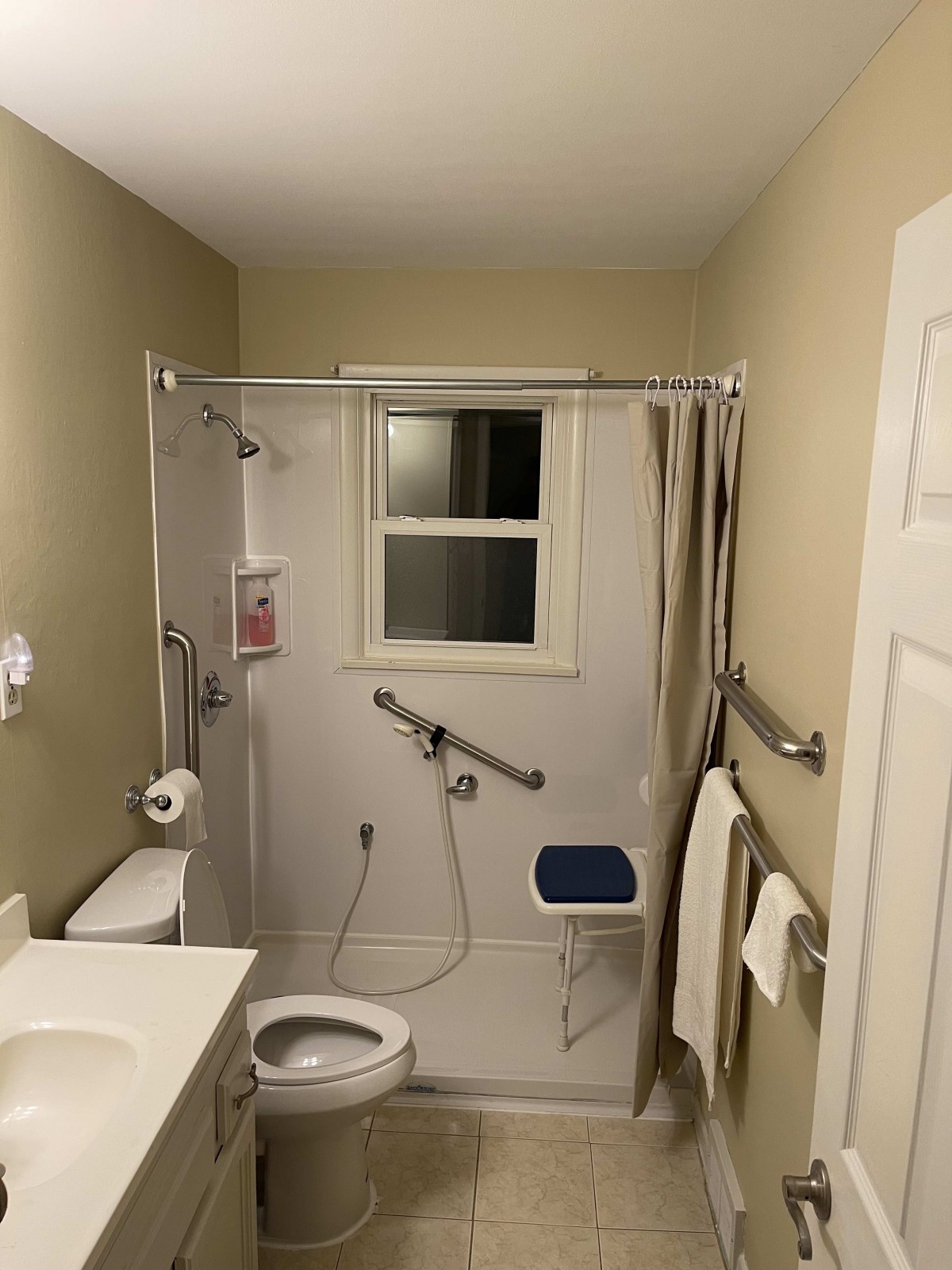 An accessible bathroom with a shower equipped with grab bars and a foldable seat.