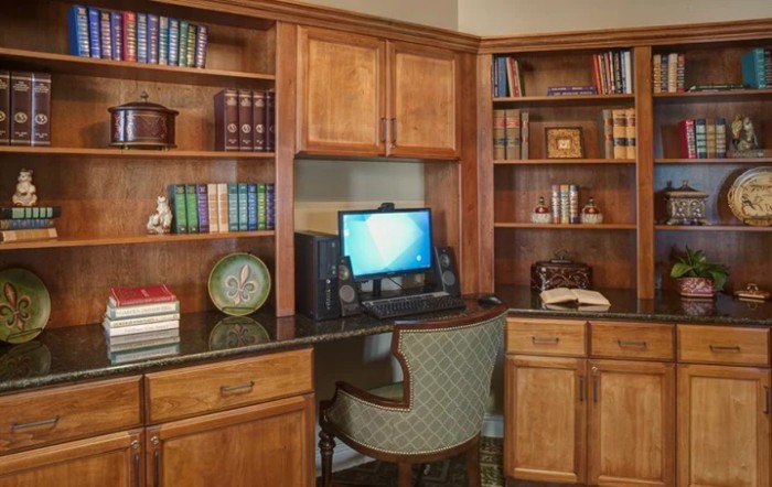 A cozy home office with a wooden desk, computer, and bookshelves filled with books.