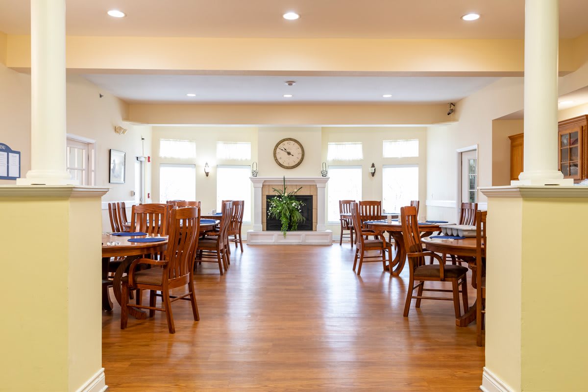 A spacious dining room with wooden tables and chairs, featuring a fireplace and large windows allowing natural light.