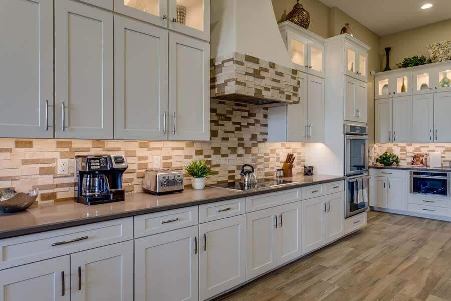 A modern kitchen with white cabinets, a stylish backsplash, and various appliances on the countertop.