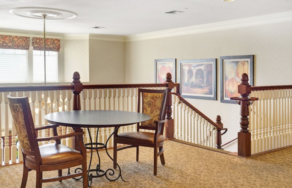 A cozy interior space featuring a small table and chairs near a stair railing, adorned with framed artwork on the walls.