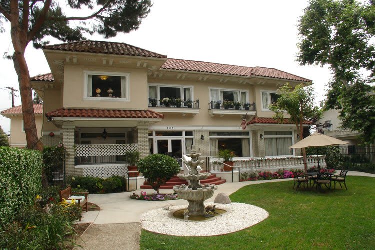 A large two-story house with a beautiful garden and fountain in the front yard.