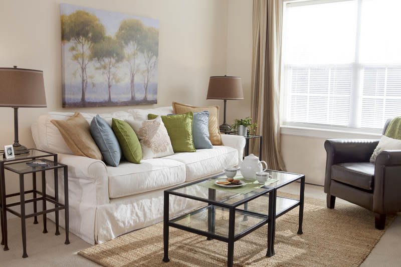 A cozy living room with a white sofa, colorful pillows, and a glass coffee table.