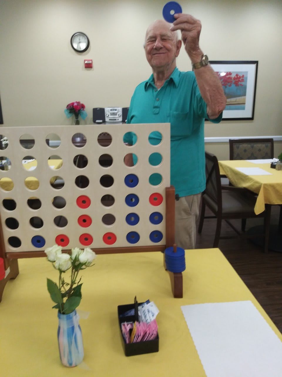 A person playing a game of Connect Four on a table indoors, with flowers as decoration.