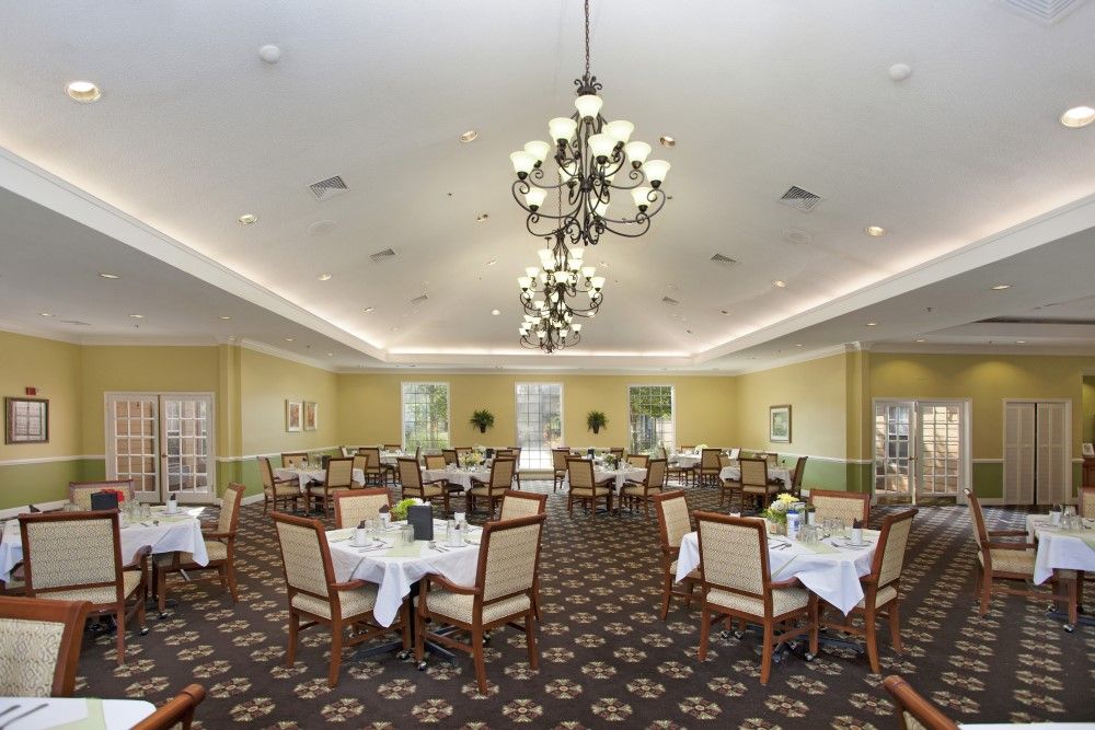 A spacious dining room with elegant chandeliers and neatly arranged tables and chairs, set in a formal style.