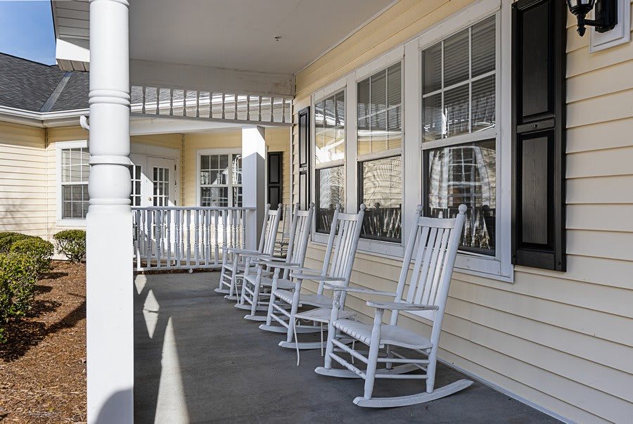 A row of white rocking chairs on a sunny porch.