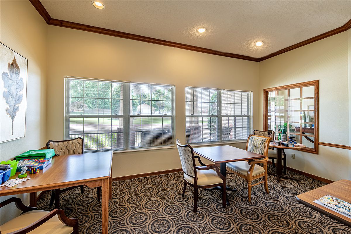 A bright dining area with tables and chairs, featuring large windows and decorative carpeting.