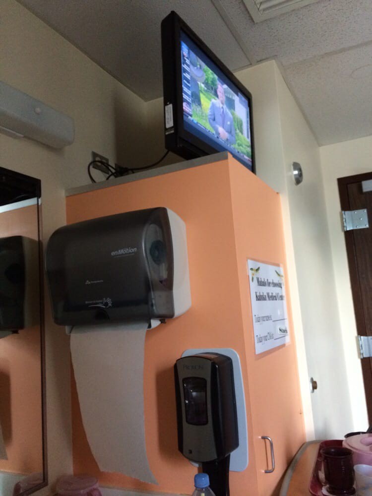 A bathroom corner featuring a hand dryer, a wall-mounted TV, and a dispenser.