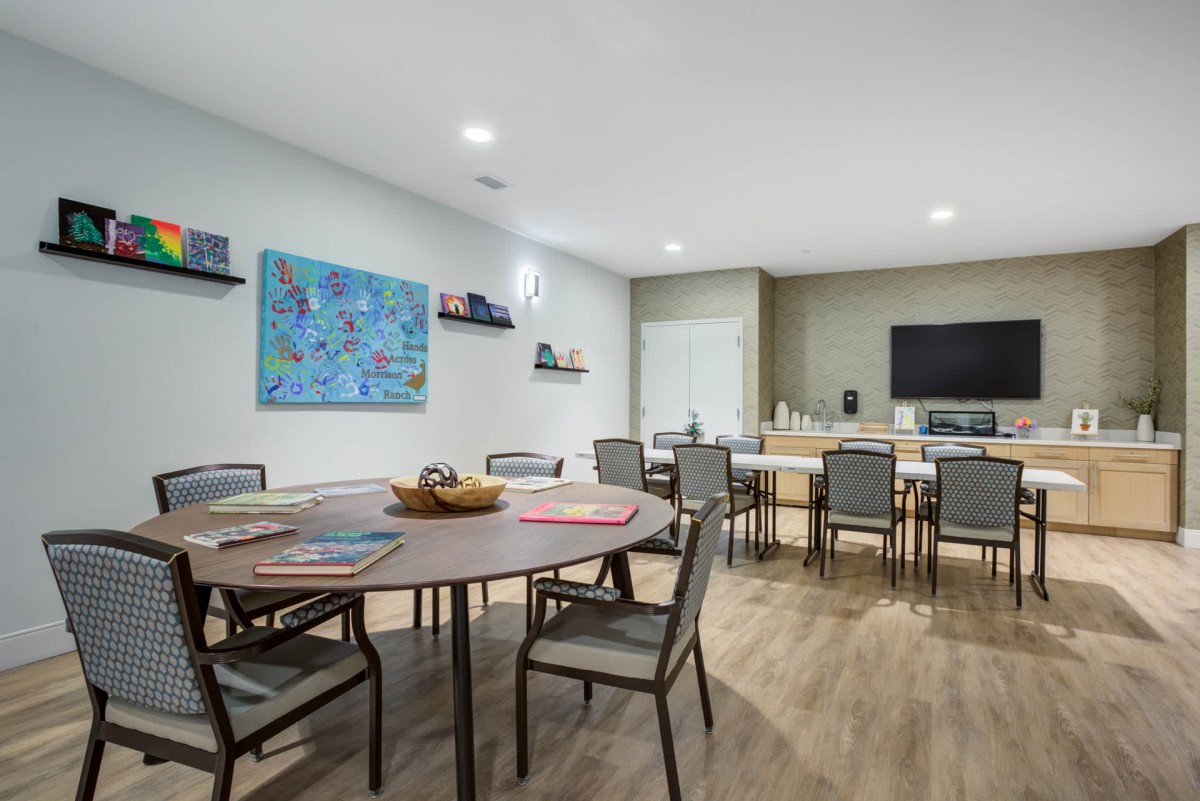 A modern meeting room with round tables and chairs, featuring a television and wall art.