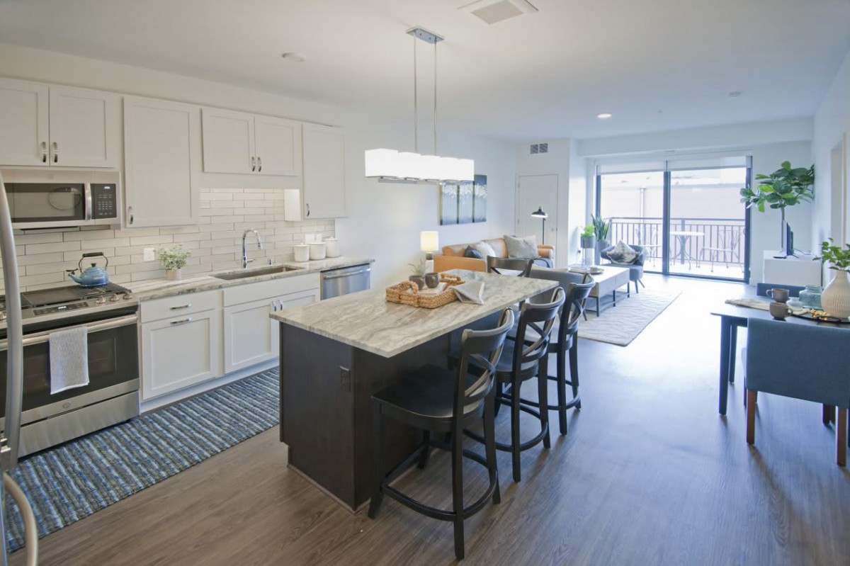 A modern open-concept kitchen with a central island and dining area, featuring bright lighting and wood flooring.