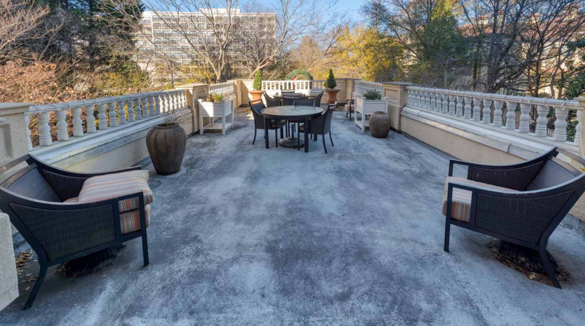 Spacious outdoor terrace with furniture and potted plants under a clear sky.