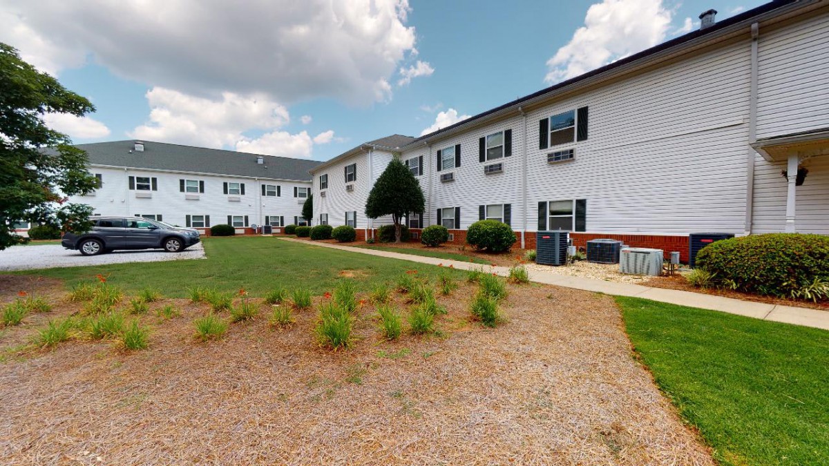 Two-story residential building with a landscaped lawn under a partly cloudy sky.