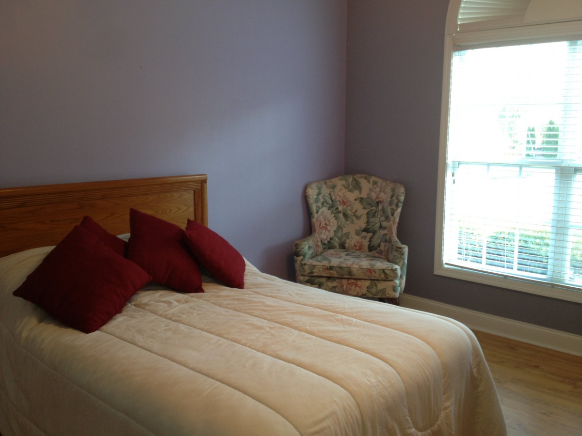A cozy bedroom with a neatly made bed and an accent chair by the window.
