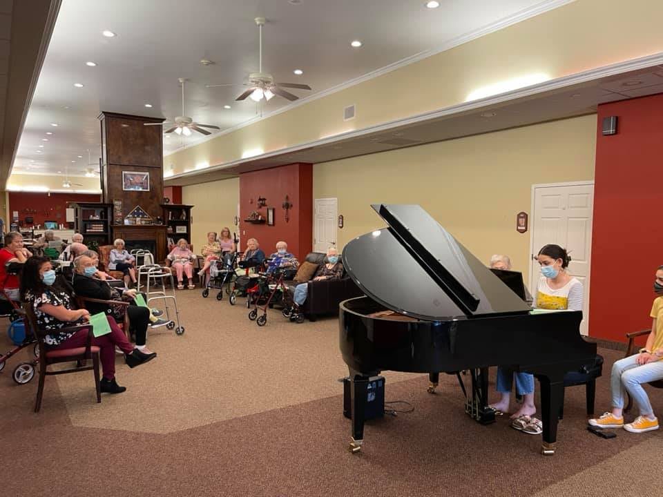 A pianist performs in front of an attentive audience in a cozy indoor setting.
