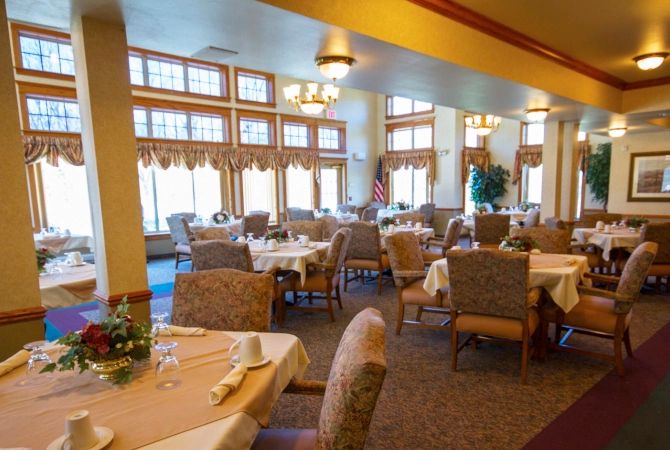 A cozy dining area in a restaurant with neatly arranged tables and chairs, large windows, and soft lighting.