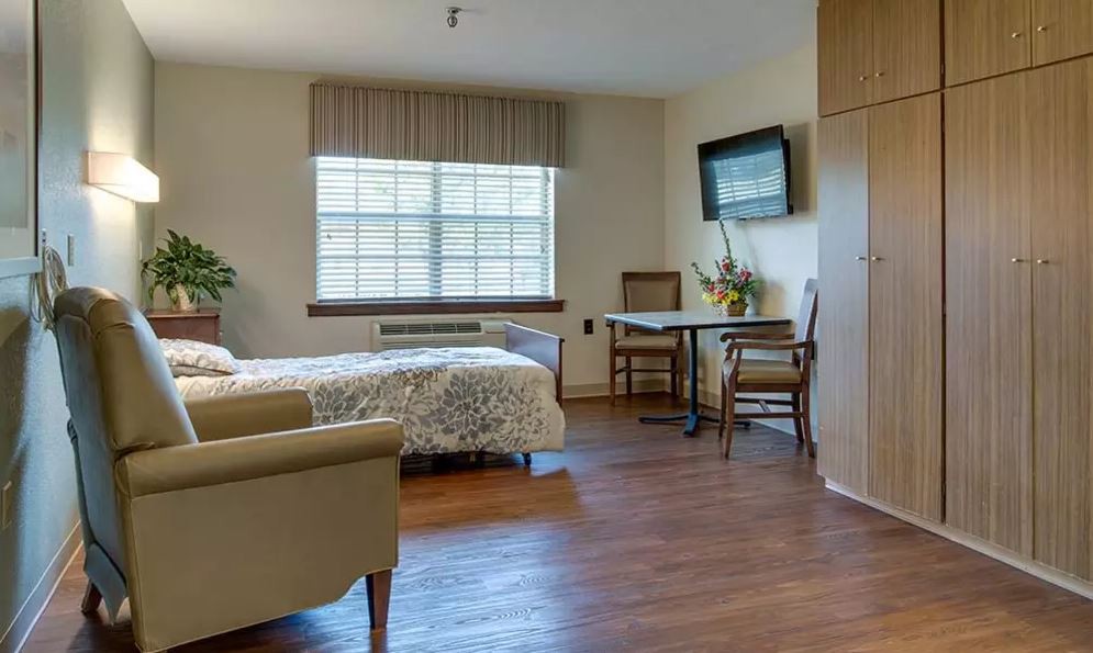 A cozy bedroom with a bed, chairs, table, and a wall-mounted TV.