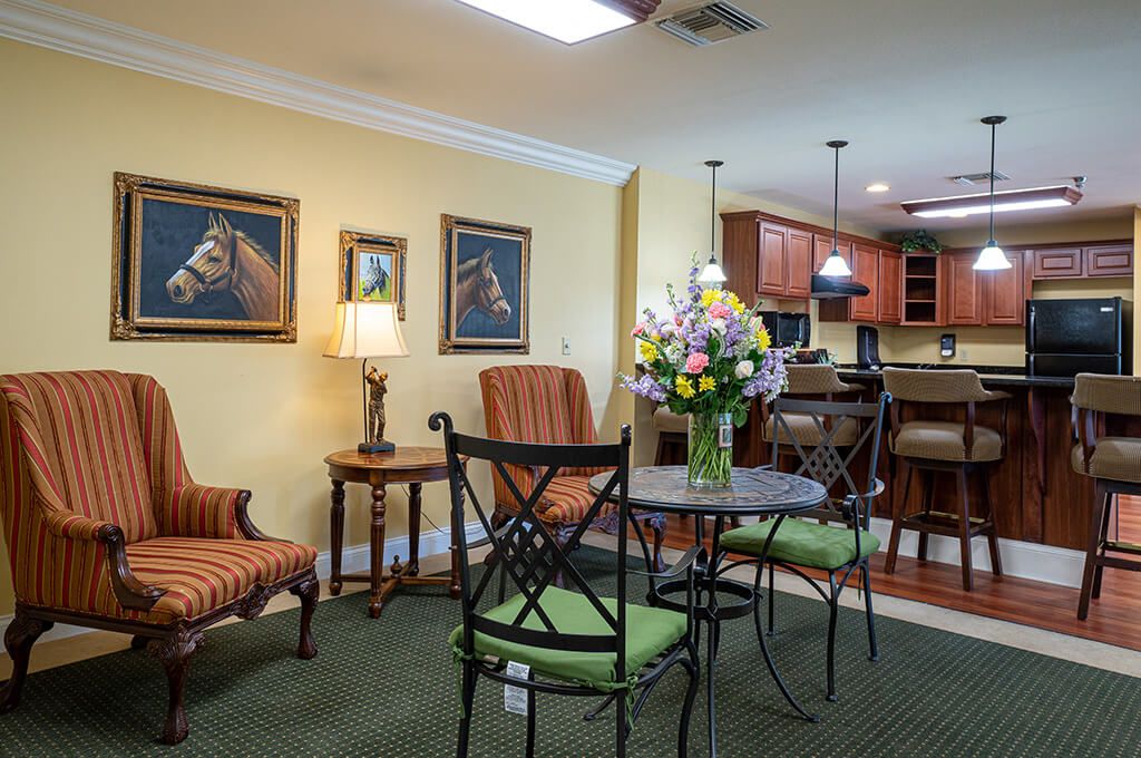 A cozy living room with a small dining table, surrounded by comfortable seating and decorated with paintings and fresh flowers.