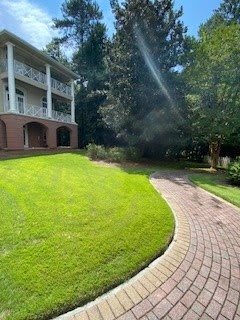 A large house with a well-manicured lawn and a brick driveway leading towards it on a sunny day.