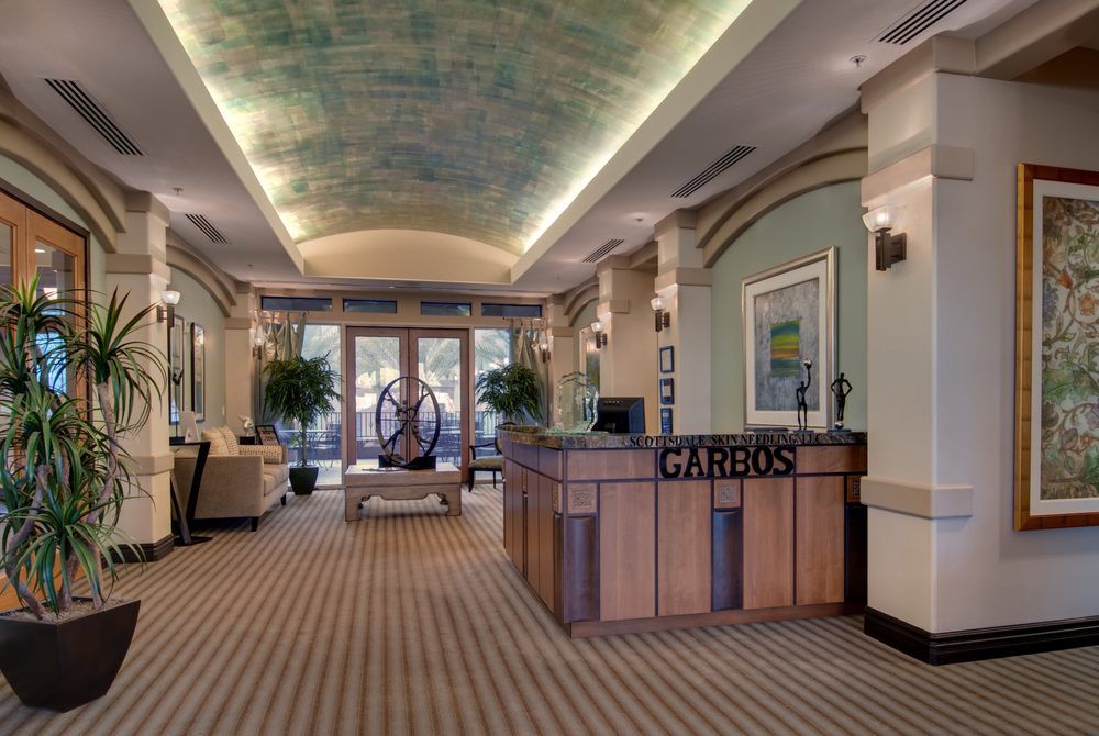 A stylish and welcoming reception area with a wooden desk, elegant ceiling design, artwork, and potted plants.