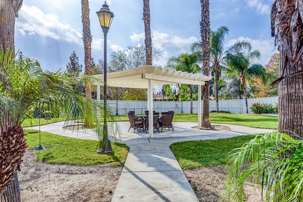 A tranquil garden setting featuring a gazebo with outdoor seating, surrounded by palm trees and a well-maintained walkway.