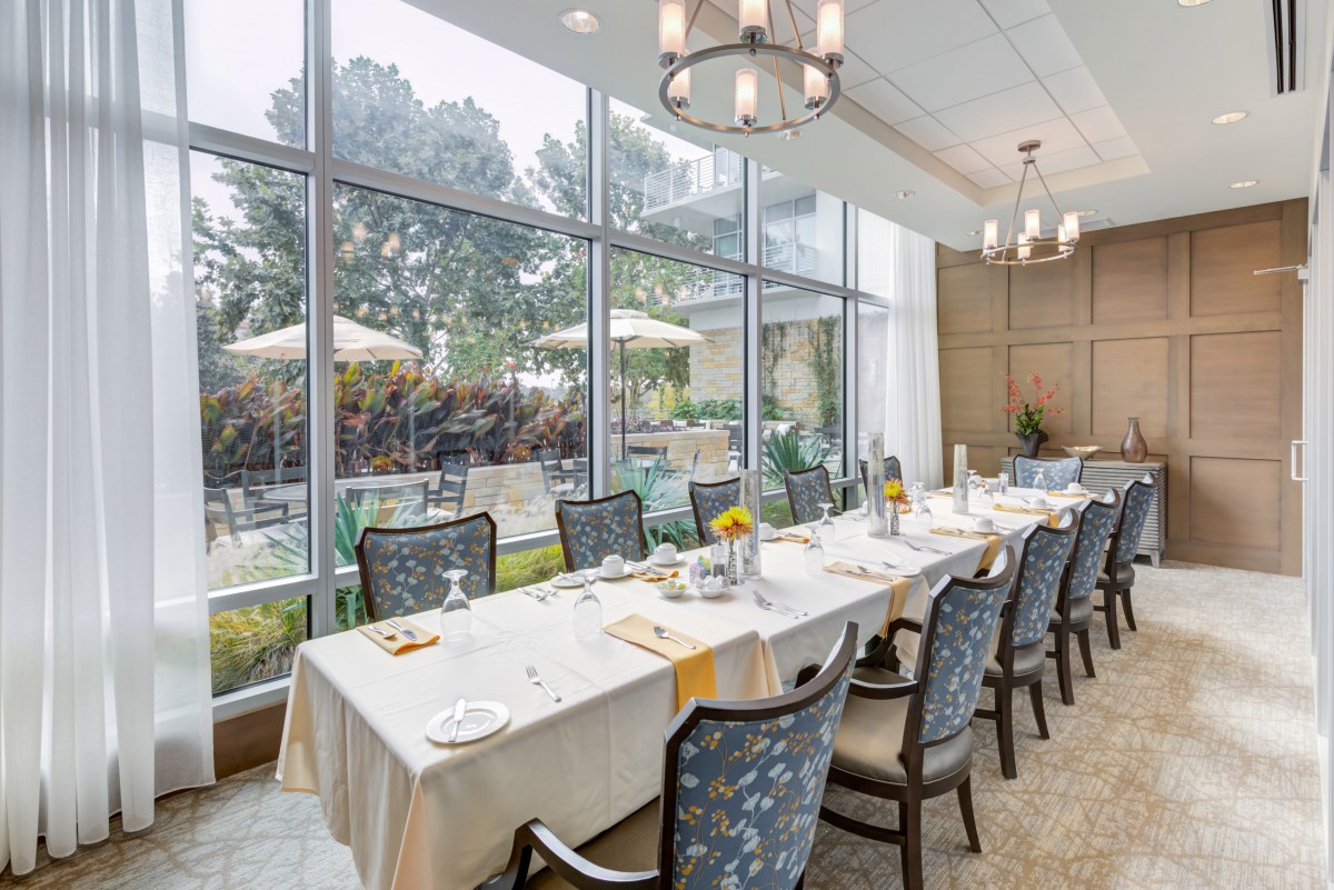 A beautifully set dining table in a bright room with large windows overlooking a garden.