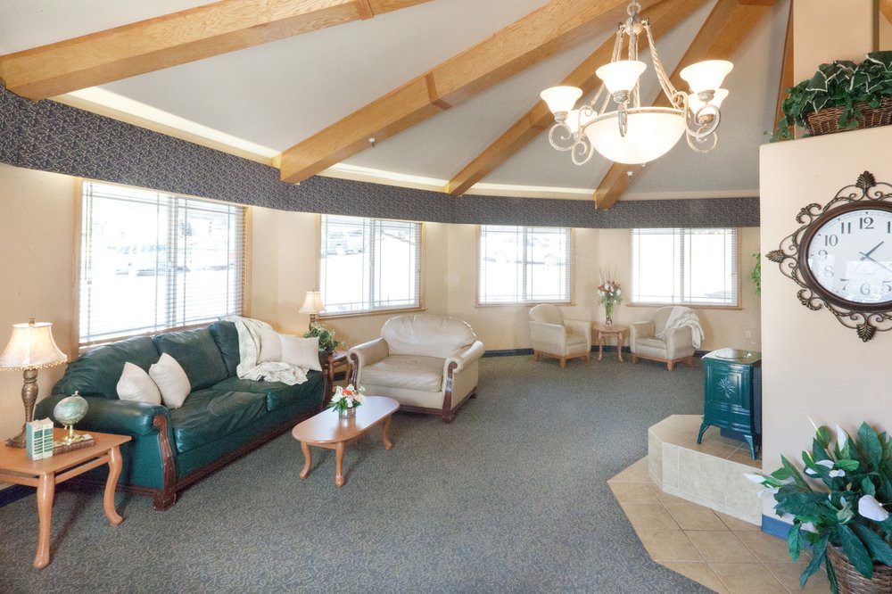 A spacious living room with a circular layout, featuring multiple sofas and chairs, a coffee table, large windows, and a chandelier.