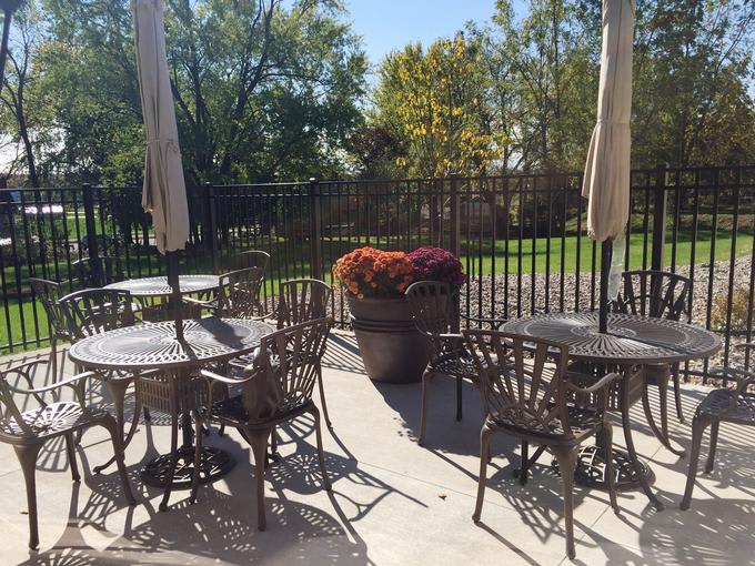 A sunny patio with metal tables and chairs, surrounded by a fence and potted plants.