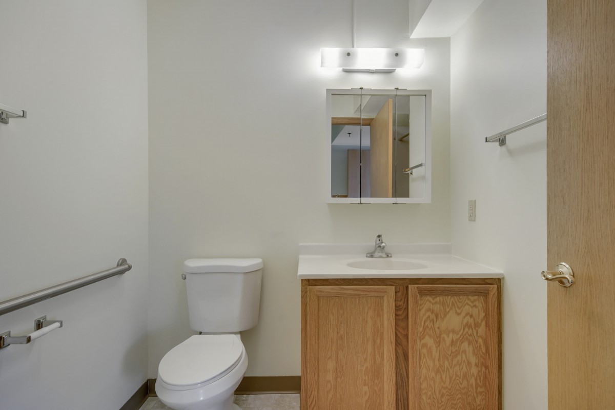 A simple bathroom with a toilet, sink, and mirror under bright lighting.