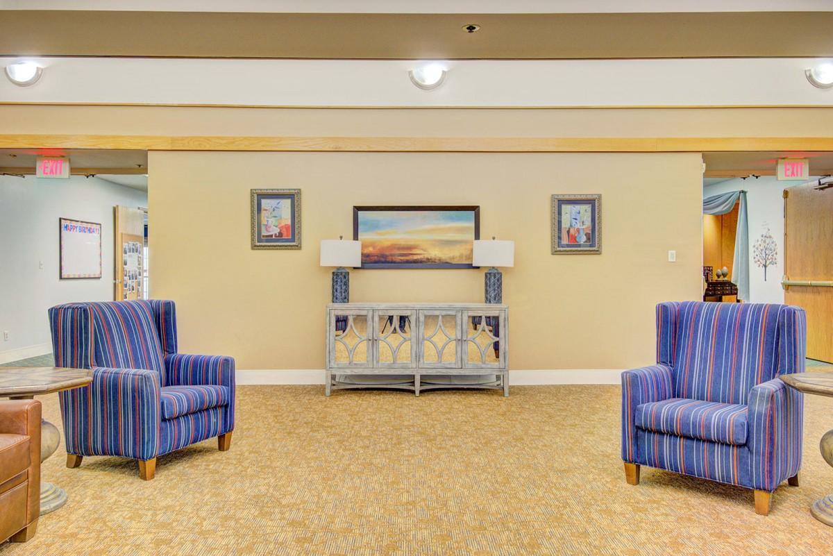 A cozy living room with blue armchairs, decorative paintings, and a carpeted floor.