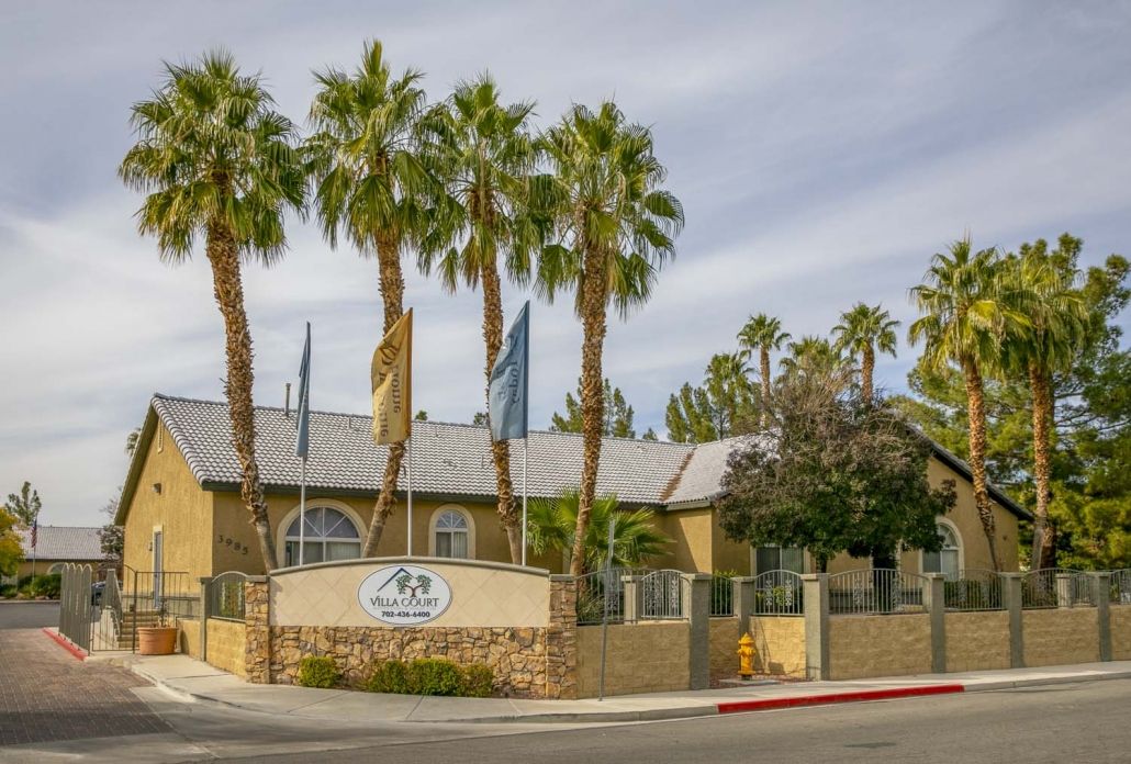 A residential apartment building with palm trees at the street corner.