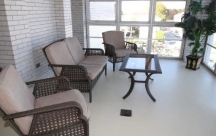 A cozy patio setup with wicker furniture and a glass-top table, surrounded by large windows.