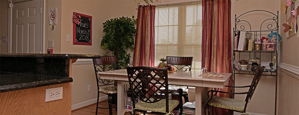 A cozy dining room with a table, chairs, and large windows adorned with curtains.