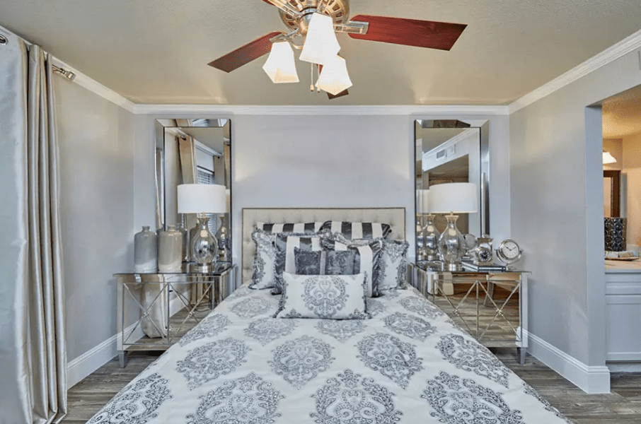 A modern bedroom with elegant patterned bedding, a ceiling fan, and symmetrical mirrored bedside tables.