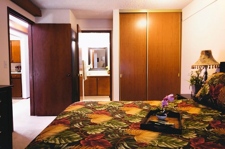 A cozy bedroom with a floral bedspread, wooden closet doors, and an open door leading to a bathroom.