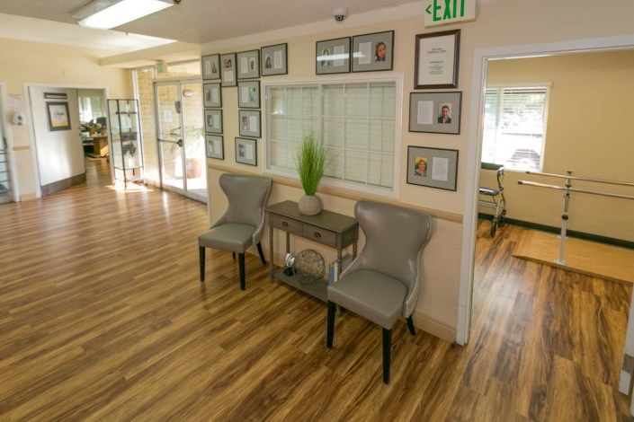 A cozy waiting area with two chairs and a small table, accented by decorative plants and framed pictures on the wall.