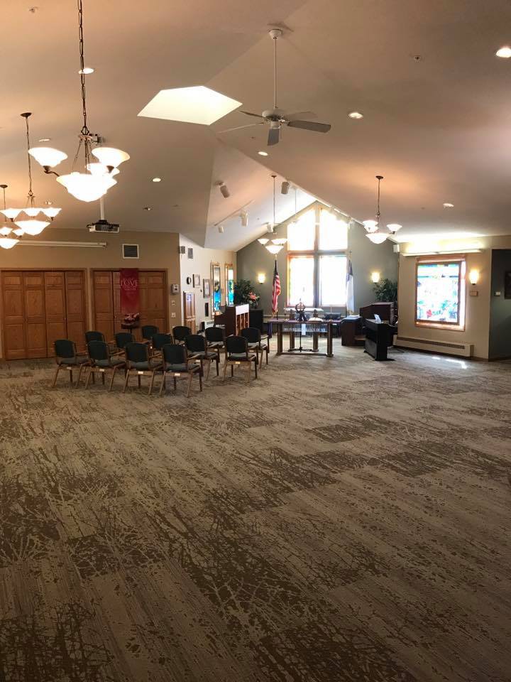 A spacious interior of a community center with chairs arranged in a circle and large windows providing natural light.