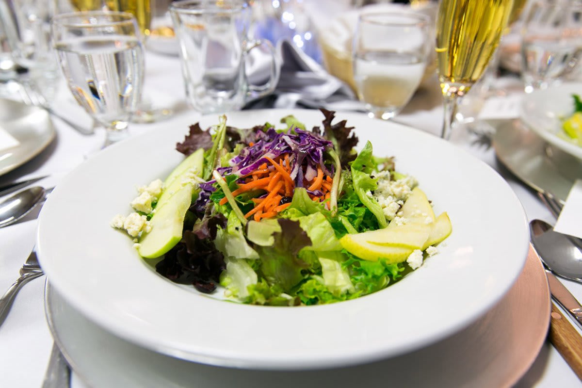 A fresh garden salad with mixed greens, sliced avocado, and shredded carrots, served on a white plate.