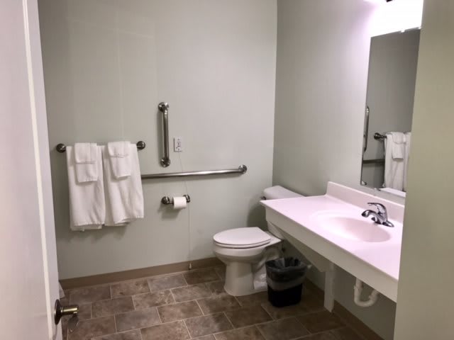 An accessible bathroom featuring a toilet, sink, grab bars, and towels.