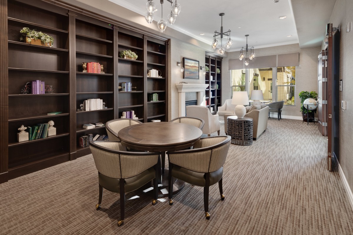 A modern library interior featuring dark bookshelves, a round table with chairs, and stylish lighting.