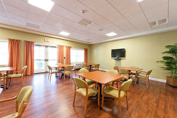 A well-lit dining area with tables and chairs, featuring a television on the wall and wooden flooring.