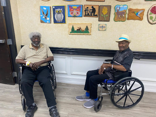 Two elderly men enjoying each other's company in a community center, surrounded by vibrant artwork.