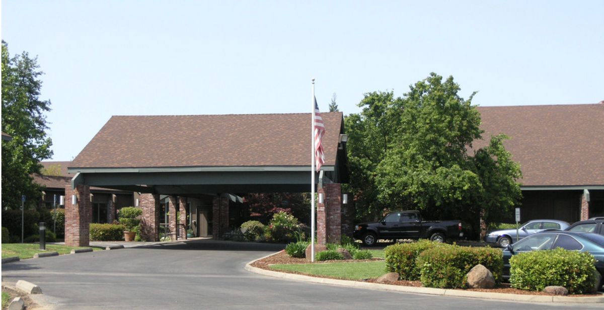 A building entrance with a flagpole and surrounding trees and landscaping.