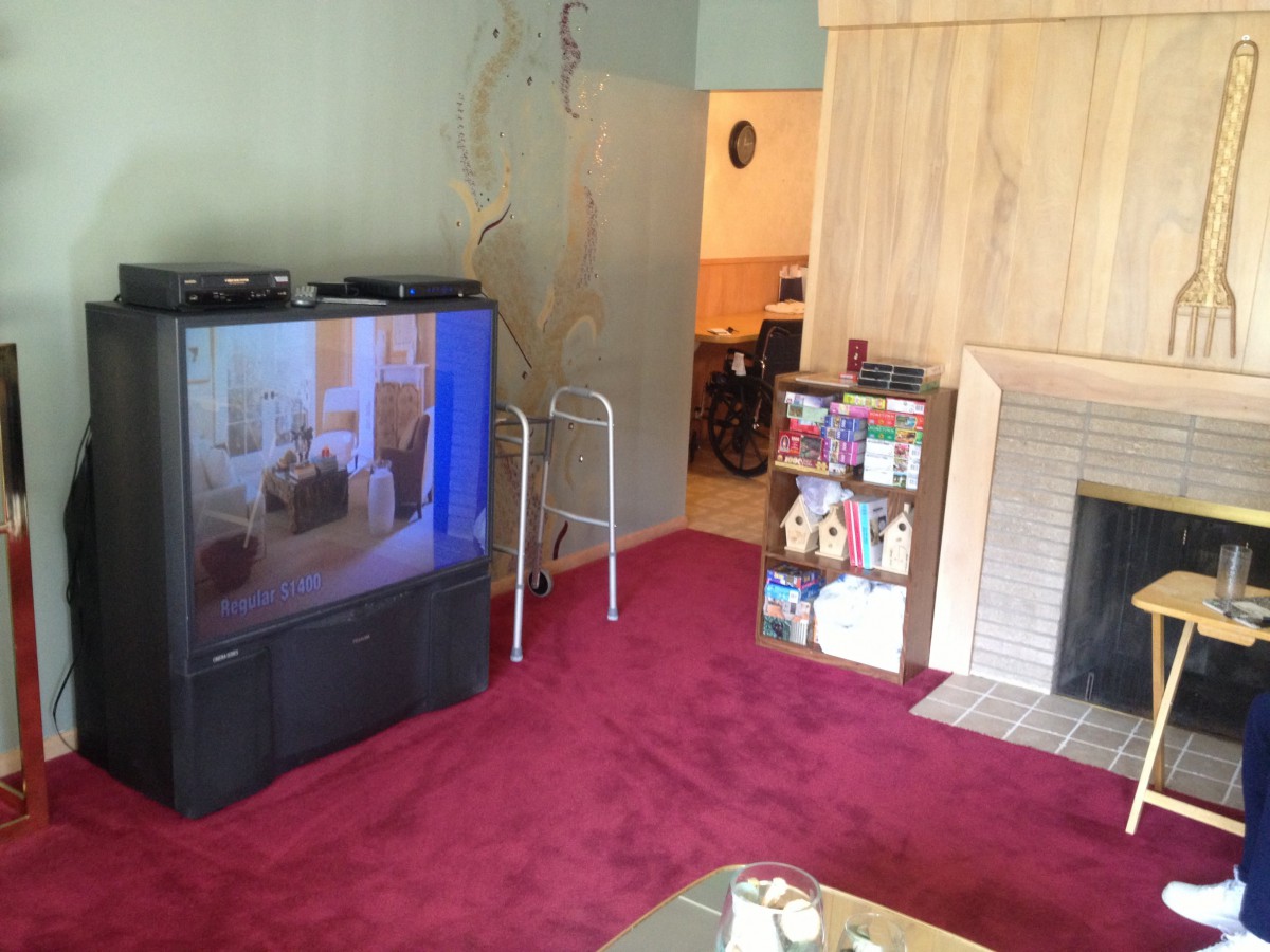 A cozy living room with a large television, red carpet, and a fireplace.
