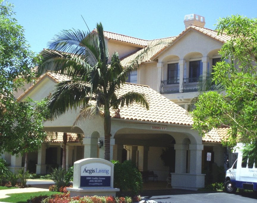 A two-story residential building with a tiled roof, surrounded by palm trees.